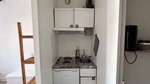 Una kitchenette compacta con estufa, lavamanos y refrigerador pequeño.