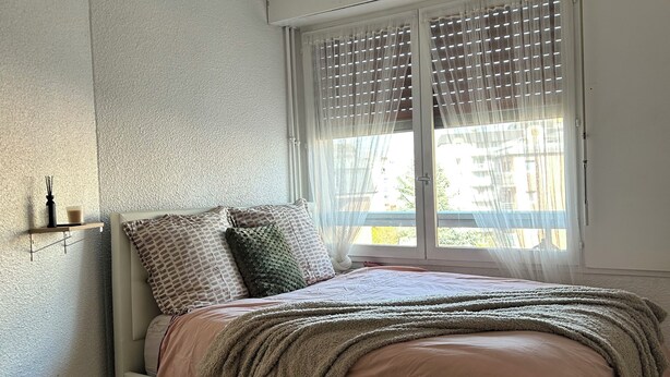 Un dormitorio con una cama, una ventana con persianas y suelo de madera.