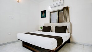 A modern bedroom with a large bed, a window with curtains, an air conditioning unit, and a small plant on the nightstand. - AYUSHMAAN- Premium (Jabalpur)