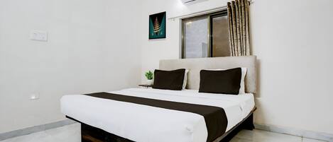 A modern bedroom with a large bed, a window with curtains, an air conditioning unit, and a small plant on the nightstand.