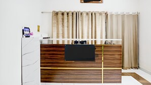 A room with a bed, a bedside table, a mirror, a window with curtains, and a wall-mounted shelf. - AYUSHMAAN- Premium (Jabalpur)