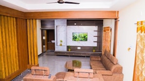 A modern living room with a sofa set, a coffee table, and a flat-screen TV mounted on a marble wall. - Sanskriti Homestay (Tirupati)