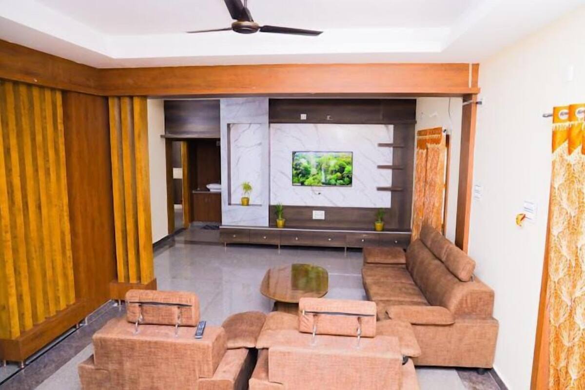A modern living room with a sofa set, a coffee table, and a flat-screen TV mounted on a marble wall.