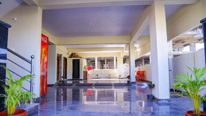 A spacious lobby with a polished marble floor, a Coca-Cola advertisement, and a seating area with red chairs. - Sanskriti Homestay (Tirupati)