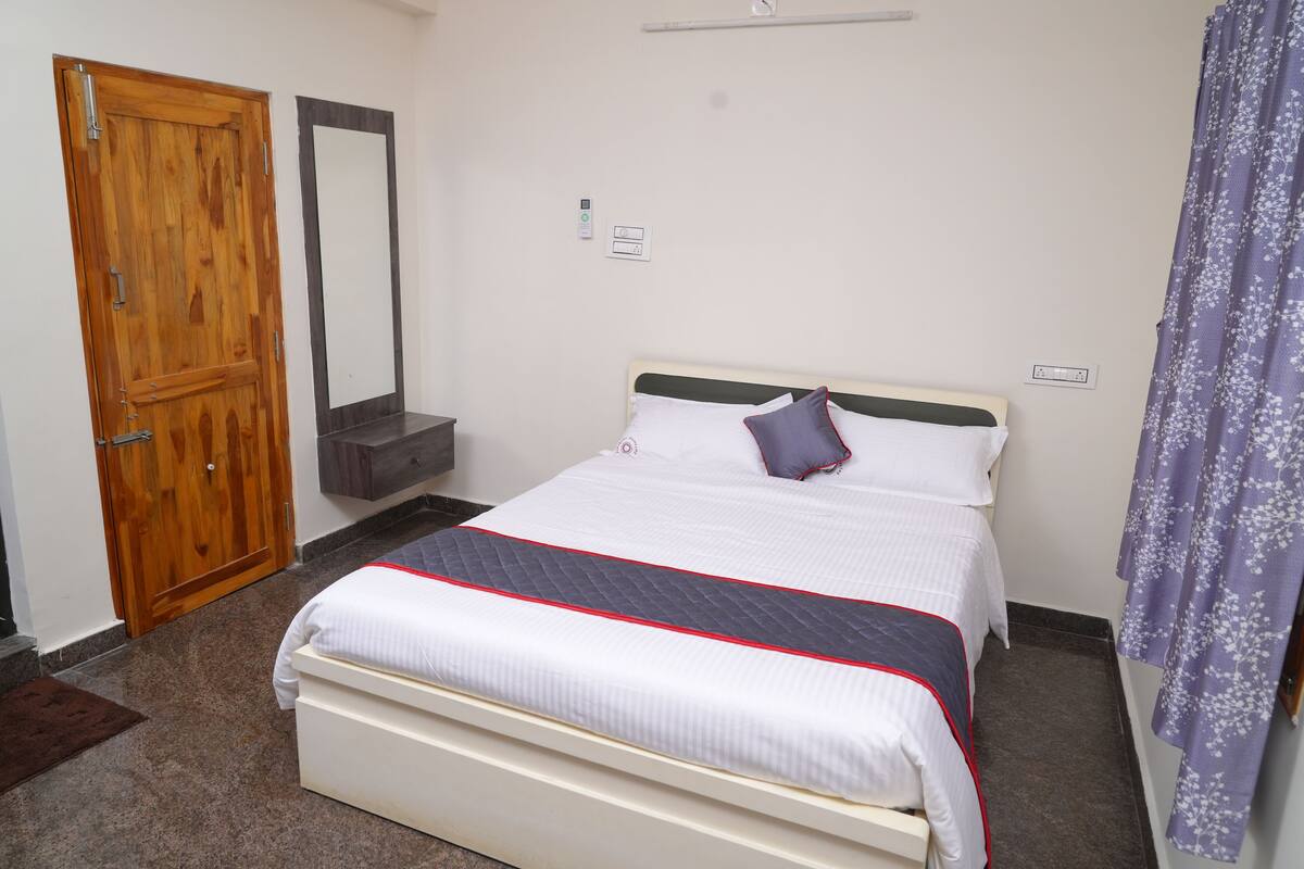 A bedroom with a bed, a wooden door, a mirror, and a bathroom.