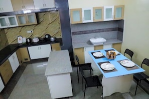 A compact kitchen with a marble backsplash, a sink, and a dining area with a blue tablecloth and chairs.