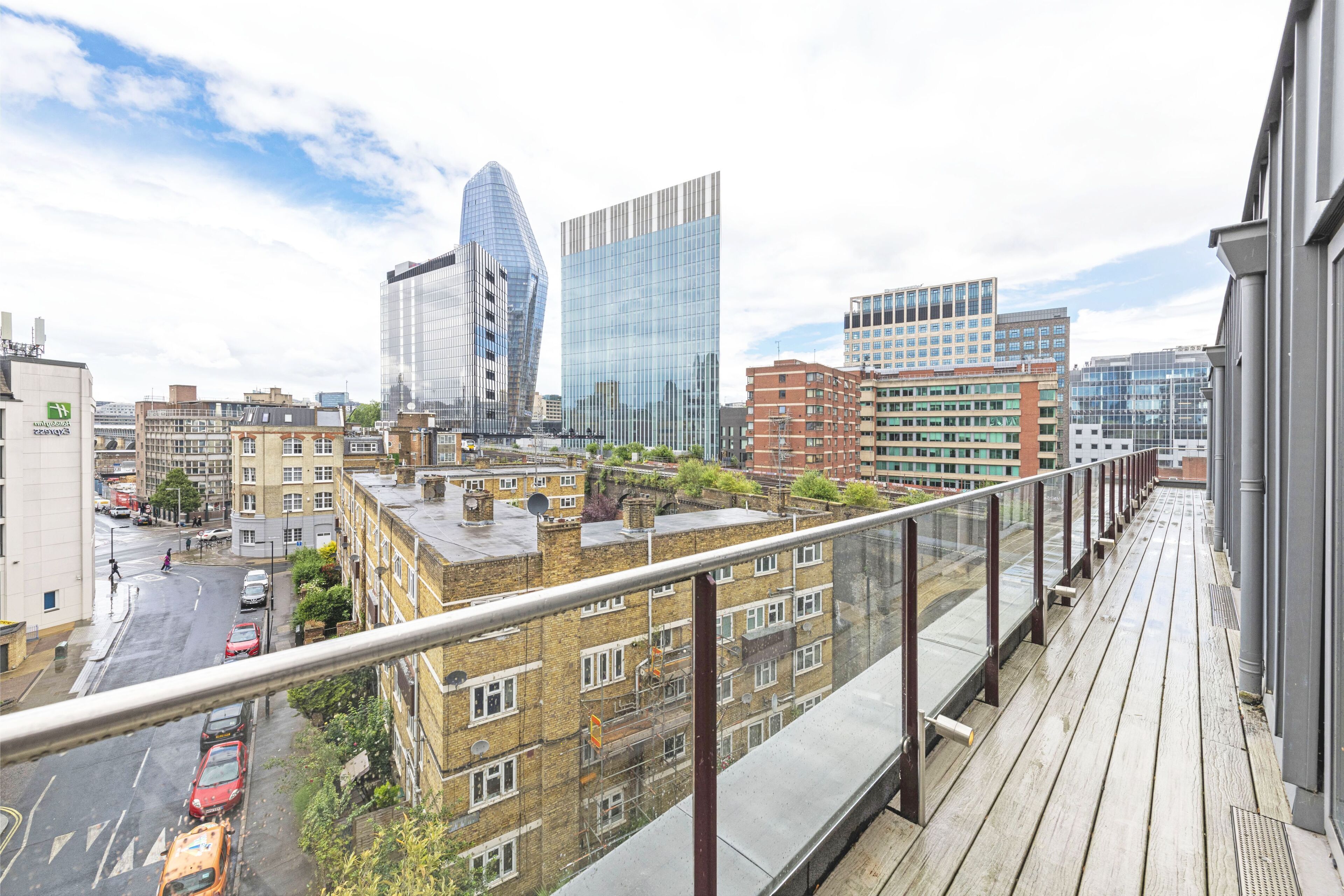 A balcony with a view of a cityscape, including modern buildings and a road with cars.