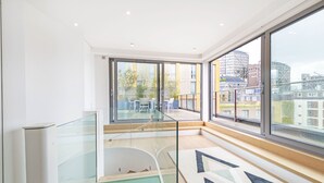 Un appartement moderne doté de grandes fenêtres, d’une balustrade en verre et offrant une vue sur la ville.