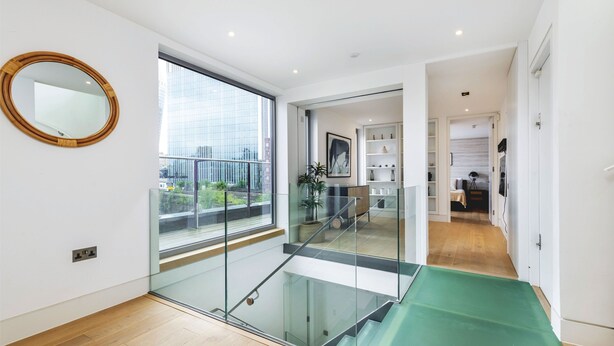Un intérieur moderne avec un escalier en verre, une grande fenêtre donnant sur la ville et un design minimaliste caractérisé par des murs blancs et un plancher en bois.