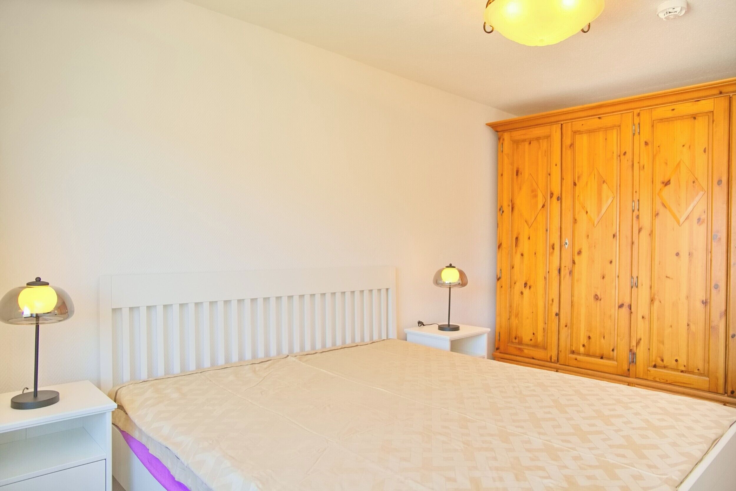 Ein Schlafzimmer mit einem Bett, zwei Nachttischlampen, einem weißen Nachttisch und einem Holzschrank.
