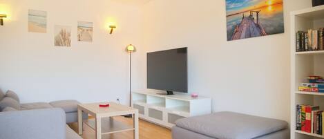 A modern living room with a flat-screen TV, a bookshelf, and a painting of a sunset.