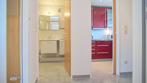 Una cucina moderna con mobili bianchi e dettagli rossi, un microonde a vista e un pavimento piastrellato.