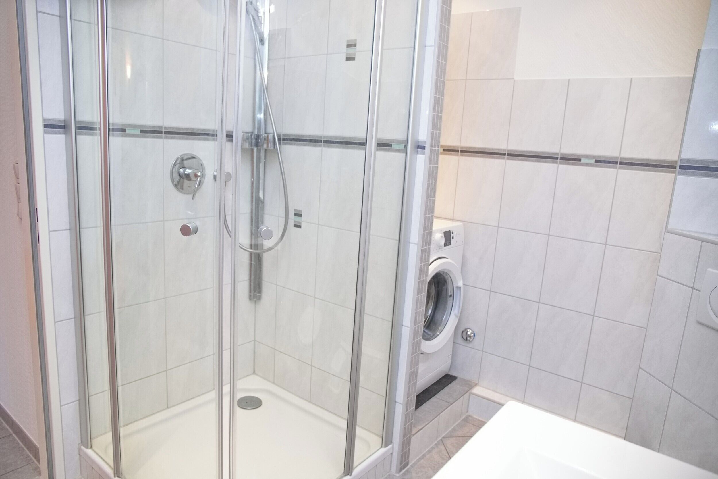 Une douche fermée par des parois en verre, dotée d’un pommeau de douche à main et d’un robinet mural.