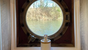 A window with a circular porthole design, a wooden frame, and a white vase in front. - Péniche Le Pescalune (Arles)
