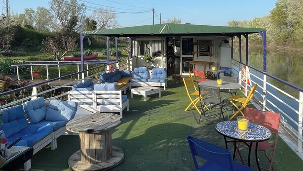 An outdoor patio with seating and tables, a covered area, and a view of a water body. - Péniche Le Pescalune (Arles)