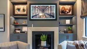 A living room with a fireplace, two armchairs, a coffee table, and bookshelves with decorative items.