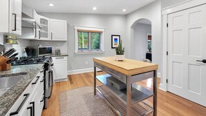 A modern kitchen with white cabinets, a granite countertop, a wooden table, and a window with blinds.
