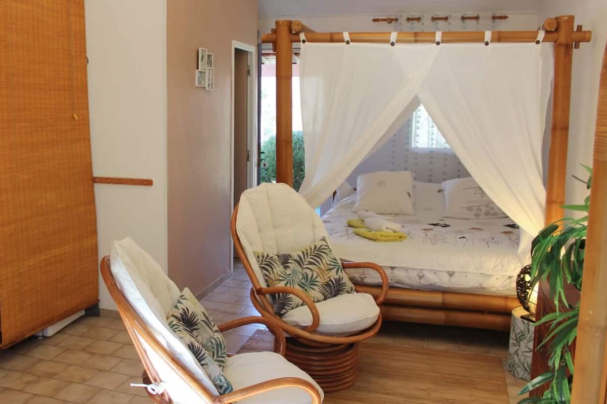 Quarto com cama, duas cadeiras de vime, mesa de cabeceira e dossel.