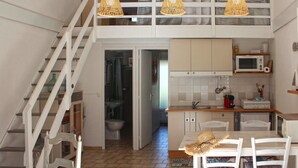 Eine Küche mit weißen Schränken, einer Mikrowelle und einem Spülbecken. Ein Esstisch mit Stühlen und eine Treppe, die zu einer oberen Ebene führen.