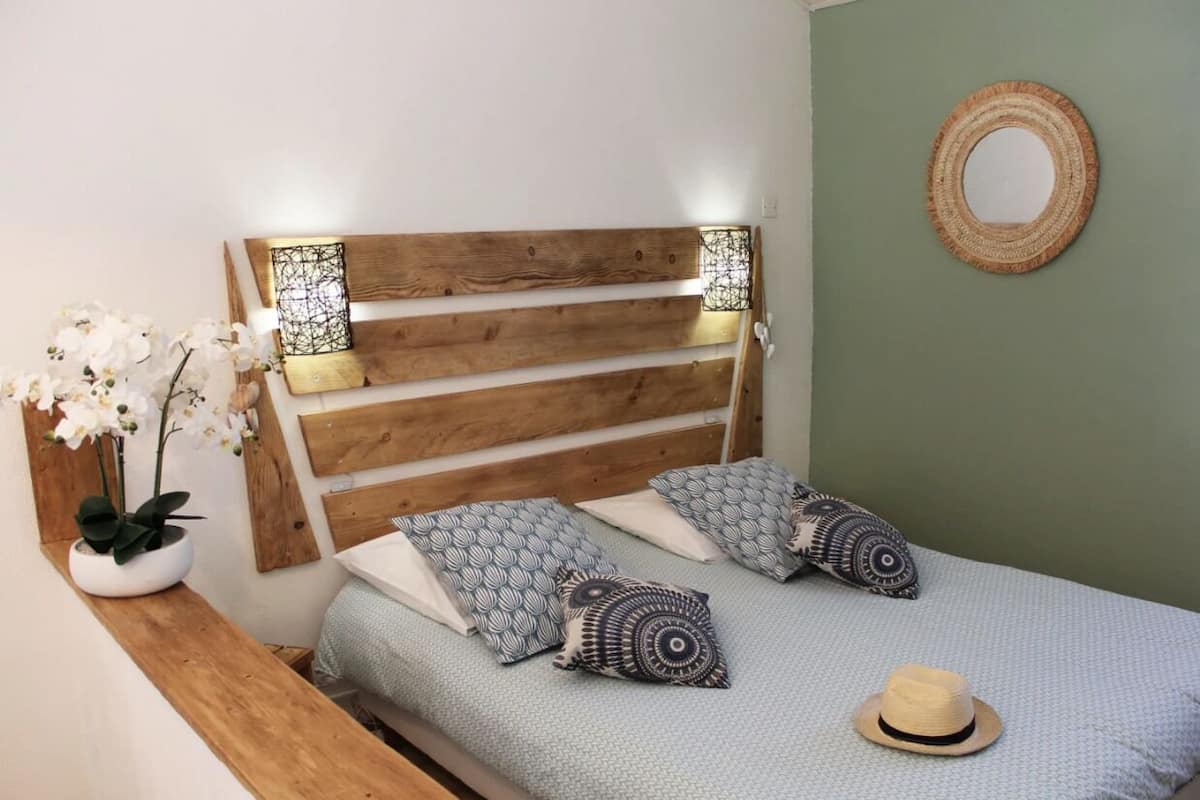 Uma cama com cabeceira de madeira, almofadas estampadas, um chapéu e um painel de parede tecido.