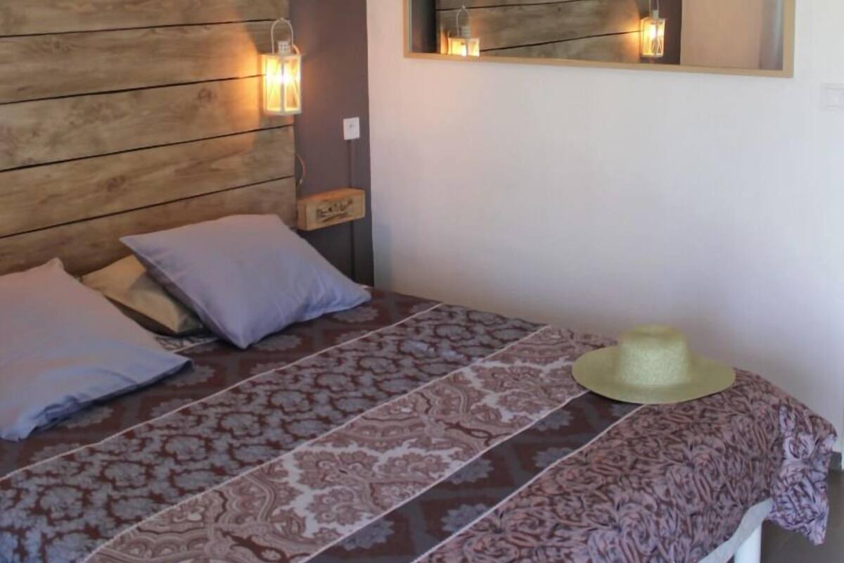 Cama com colcha estampada, duas almofadas, um chapéu e luminárias fixadas na parede.