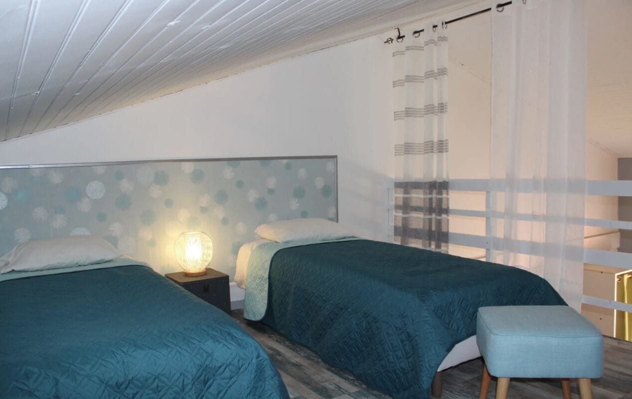 Une chambre avec deux lits, une table de chevet avec une lampe, une fenêtre avec des rideaux et un plancher en bois.