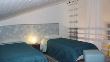Une chambre avec deux lits, une table de chevet avec une lampe, une fenêtre avec des rideaux et un plancher en bois.