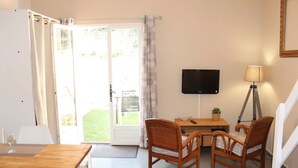 Ein Zimmer mit Holztisch, Korbstühlen, einem Fernseher an der Wand und einer Lampe.
