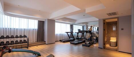 A spacious hotel gym with cardio machines, weightlifting equipment, and a mirror wall.