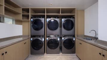 Un cuarto de lavandería con cuatro lavadoras de carga frontal, un lavabo y armarios de madera.