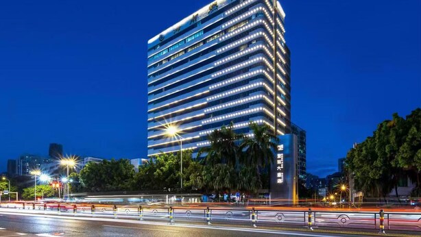 A modern high-rise building with multiple floors, illuminated windows, and a prominent sign at the top. - Dengting Hotel (Haikou)
