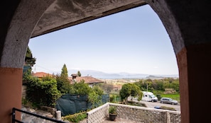 Vista desde un balcón con arco de piedra, con vistas a una zona residencial con casas, una calle y montañas a lo lejos.