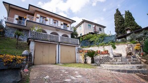 A two-story house with a garage, a balcony with potted plants, and a stone staircase leading up to the entrance.