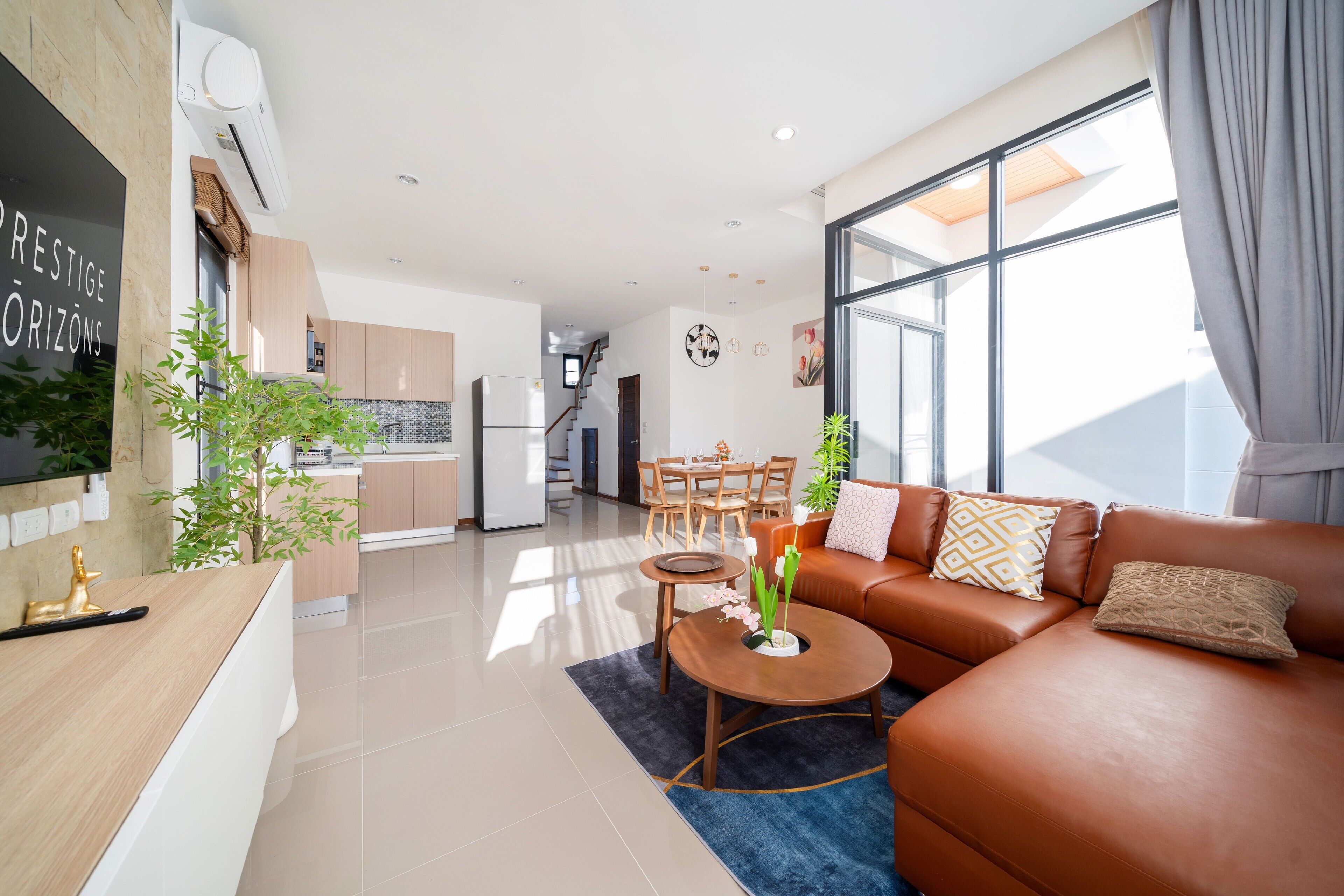 A modern living room with a brown leather sofa, a coffee table, and a dining area with wooden furniture.