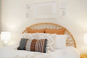 Una cama con cabecera trenzada, varios almohadones y lámparas de noche.