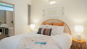 A bedroom with a bed, bedside lamps, a bedside table, a wall-mounted shelf, and a door leading to another room.