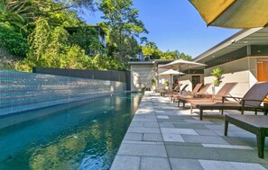 Una piscina amb gandules i sombreretes, envoltada de vegetació i un edifici modern.