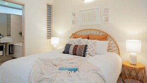 Une chambre à coucher comprenant un lit, des lampes de chevet, une table de chevet, une étagère murale et une porte donnant accès à une salle de bain.