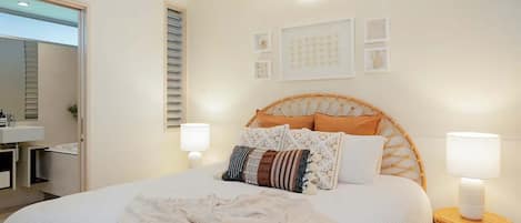 Un dormitorio con una cama, lámparas de noche, una mesita de noche, un estante en la pared y una puerta que da al baño.