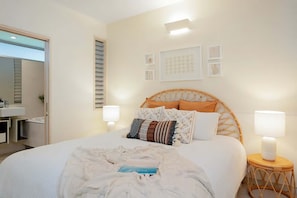 Ein Schlafzimmer mit einem Bett, Nachttischlampen, einem Nachttisch, einem Wandregal und einer Tür zu einem Badezimmer.