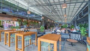 Un café intérieur doté de hauts plafonds, de tables et de chaises en bois, comprenant un bar et des espaces pour que les clients puissent s’asseoir.