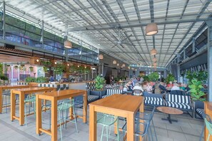 Ein Café im Inneren mit hohen Decken, Holztischen und -stühlen, inklusive einer Bar und Sitzgelegenheiten für Gäste.