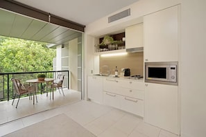 Une cuisine moderne avec des meubles blancs, un four à micro-ondes encastré et un balcon équipé d’une table et de chaises.