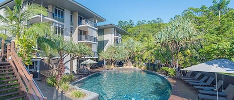 A modern hotel with a swimming pool surrounded by lush greenery and a wooden deck.