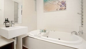 Un bany modern amb un rentapeus blanc, una banyera gran i una obra d'art a la paret amb motius de platja.