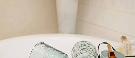 Un baño con un lavamanos blanco, un florero de vidrio con plantas verdes y un cuenco de madera pequeño con una cuchara.