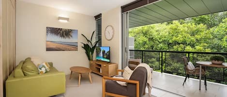 Una sala de estar moderna con un sofá, una mesa de centro, un televisor y un balcón con vistas al verdor.