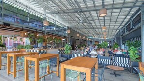 An indoor café with tables and chairs, a bar area, and a high ceiling with metal beams.