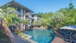 A modern hotel with a swimming pool, outdoor seating, and lush greenery.