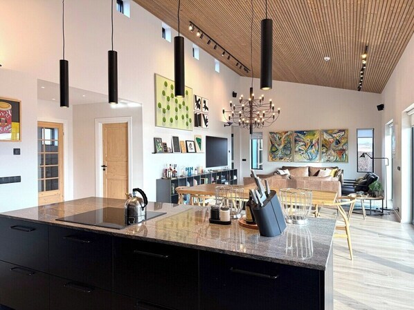 Une cuisine moderne dotée d’un grand îlot central, de meubles de couleur noire et d’un coin repas avec une table et des chaises en bois.